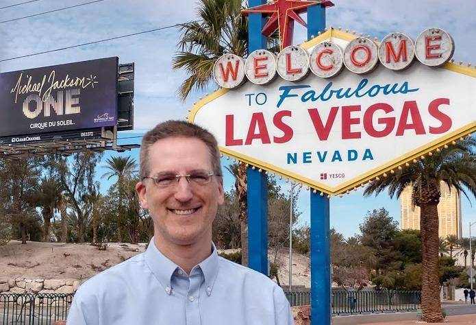 Drew Hannush living the 9-5 travel lifestyle in front of the Welcome to Las Vegas sign